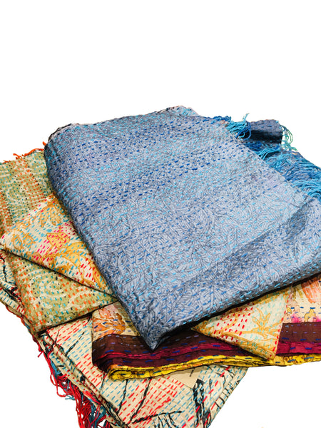 A pile of folded fair trade Kantha work scarves. The top scarf is in shades of silvery blues and purples.