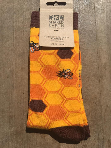 Fair trade bamboo socks with a yellow, light brown and dark brown honeycomb pattern and yellow, black and white bees and brown heels and toes. They are on a wooden background with the carboard label in place
