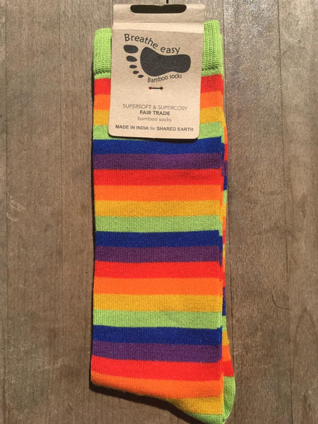 Fair trade bamboo socks with bright rainbow stripes and green heels and toes with the carboard packaging label on, laid on a wooden background