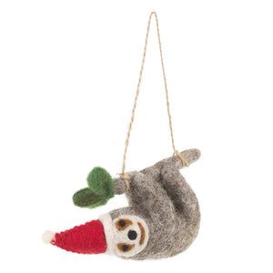 Grey felt sloth decoration hanging from a grey branch with green leaves and wearing a red Santa hat