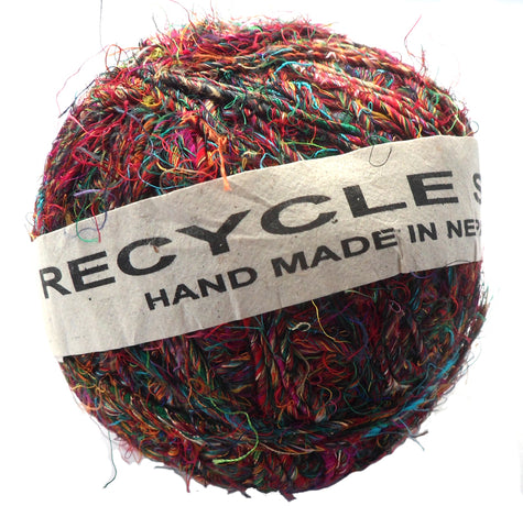 A ball of fair trade recycled sari silk yarn in shades of pink, orange, green an blue wrapped in a paper label.