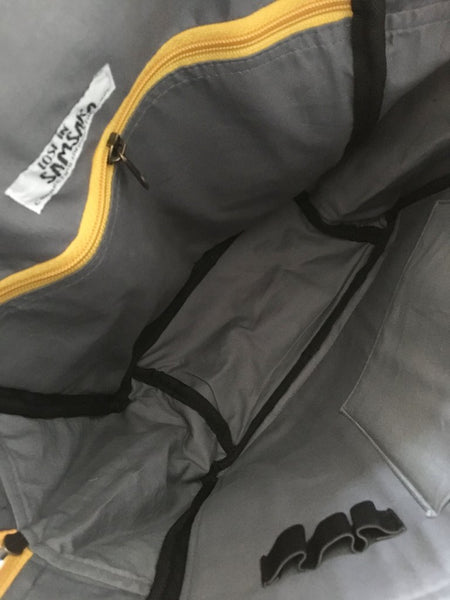 Fair trade, eco friendly, vegan backpack showing the inside view. There are multiple fabric pockets in grey material , including one with a yellow zip, and a row of three black elastic pen loops