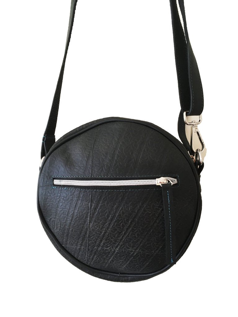 Front view of a fair trade recycled tyre round shoulder bag. The bag is black with a texture from the tyre tread and it has a silver zip.