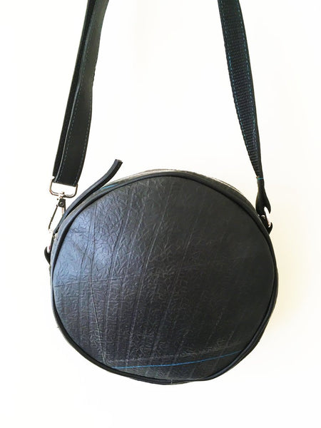 Back view of a fair trade recycled tyre round shoulder bag. The bag is black with a texture from the tyre tread and a feature line of peacock blue stitching.