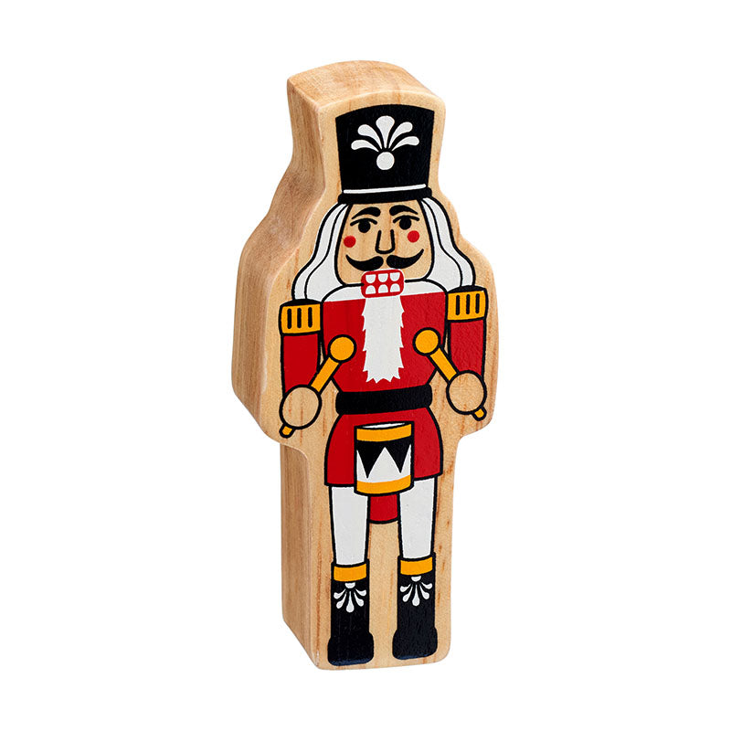 A nutcracker figure handpainted on chunky natural wood with the grain showing. He has a red coat with gold trim, black boots and hat and is holding a drum and drumsticks
