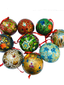 A group of traditional round baubles handpainted with floral patterns in reds, greens, blues and golds. They have a red hanging ribbon and are on a white background