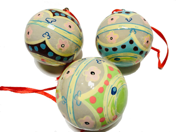 A close up view of a set of three round baubles with traditional folk patterns in shades of cream, green, pink, yellow, blue and brown. They have a red ribbon for hanging and are on a white background