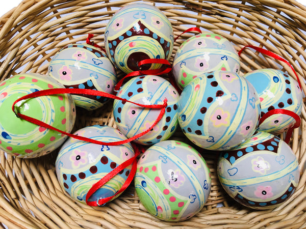 Several round baubles with traditional folk patterns in shades of cream, green, pink, yellow, blue and brown in a brown wicker basket