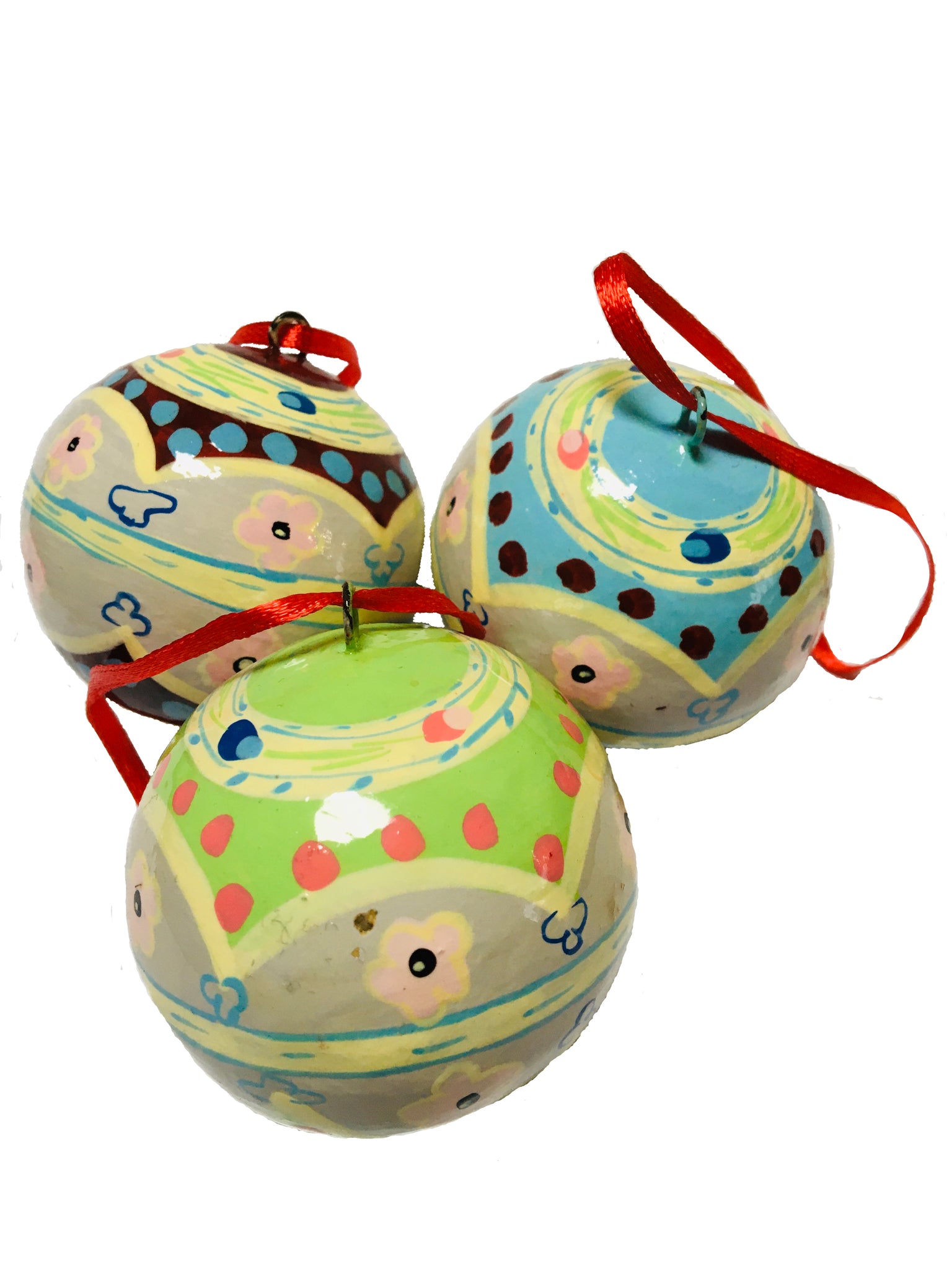 A set of three round baubles with traditional folk patterns in shades of cream, green, pink, yellow, blue and brown. They have a red ribbon for hanging and are on a white background