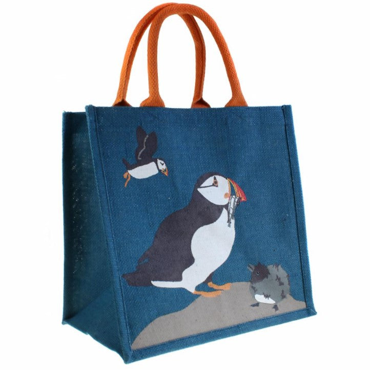 Fair trade eco-friendly jute bag in deep blue with a pattern of screen printed white, black and orange puffins on a grey rock