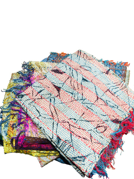 A pile of folded fair trade Kantha work scarves. The top scarf is in shades of red and blue with a black line drawing pattern overlaid.