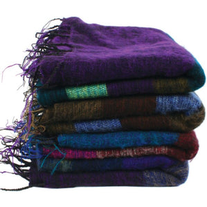 A pile of 4 fair trade recycled wool shawls. They are striped with various thickness of stripes and are shades of purple, blue, brown and green and all have tassels.
