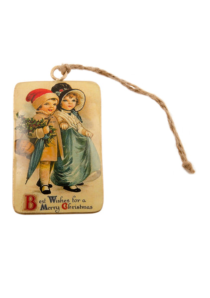 A rectangular tin Christmas decoration showing a vintage scene of a smartly dressed girl and a boy in a Santa hat carrying holly and an umbrella. Main colours are blue and gold
