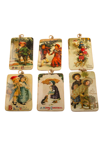 A set of six rectangular tin Christmas decorations with vintage pictures of Victorian children in festive Christmas scenes, on a white background